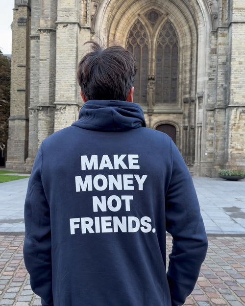 Homme de dos devant la cathédrale d'Ypres portant le pull à capuche Make Money Not Friends Hustle Wear, coloris marine