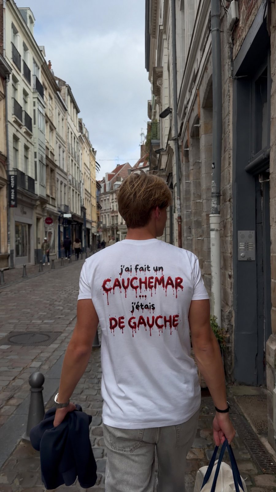 T-shirt J'ai fait un cauchemar, j'étais de gauche, édition sang, porté de dos dans une ruelle pavée, coloris blanc