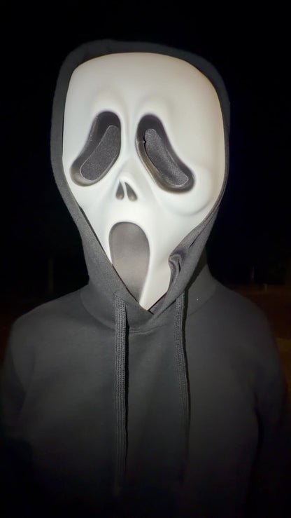 Gros plan d'un masque Scream sous une capuche, de nuit
