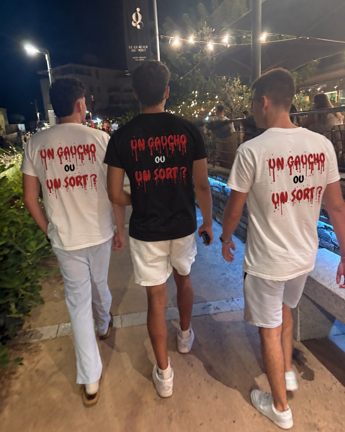 Trois amis de dos en soirée portant le t-shirt Halloween Un gaucho ou un sort, en blanc et en noir, coloris blanc et coloris noir