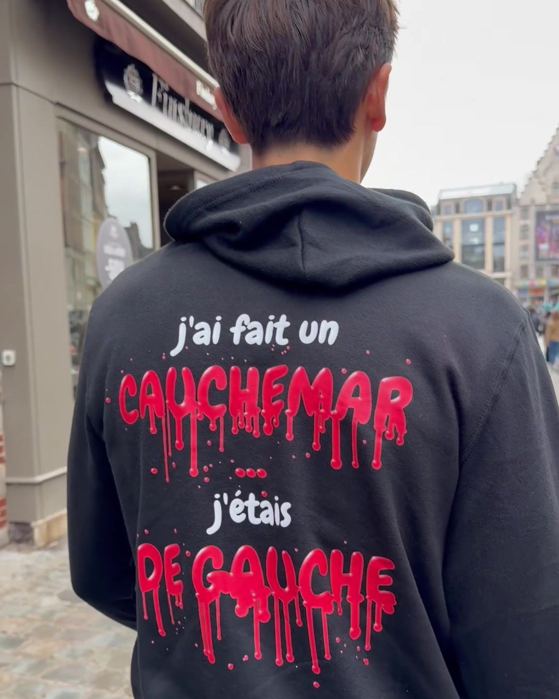 Homme de dos près de la Grand-Place de Lille portant le pull à capuche Halloween J'ai fait un cauchemar Hustle Wear, encre rouge sang