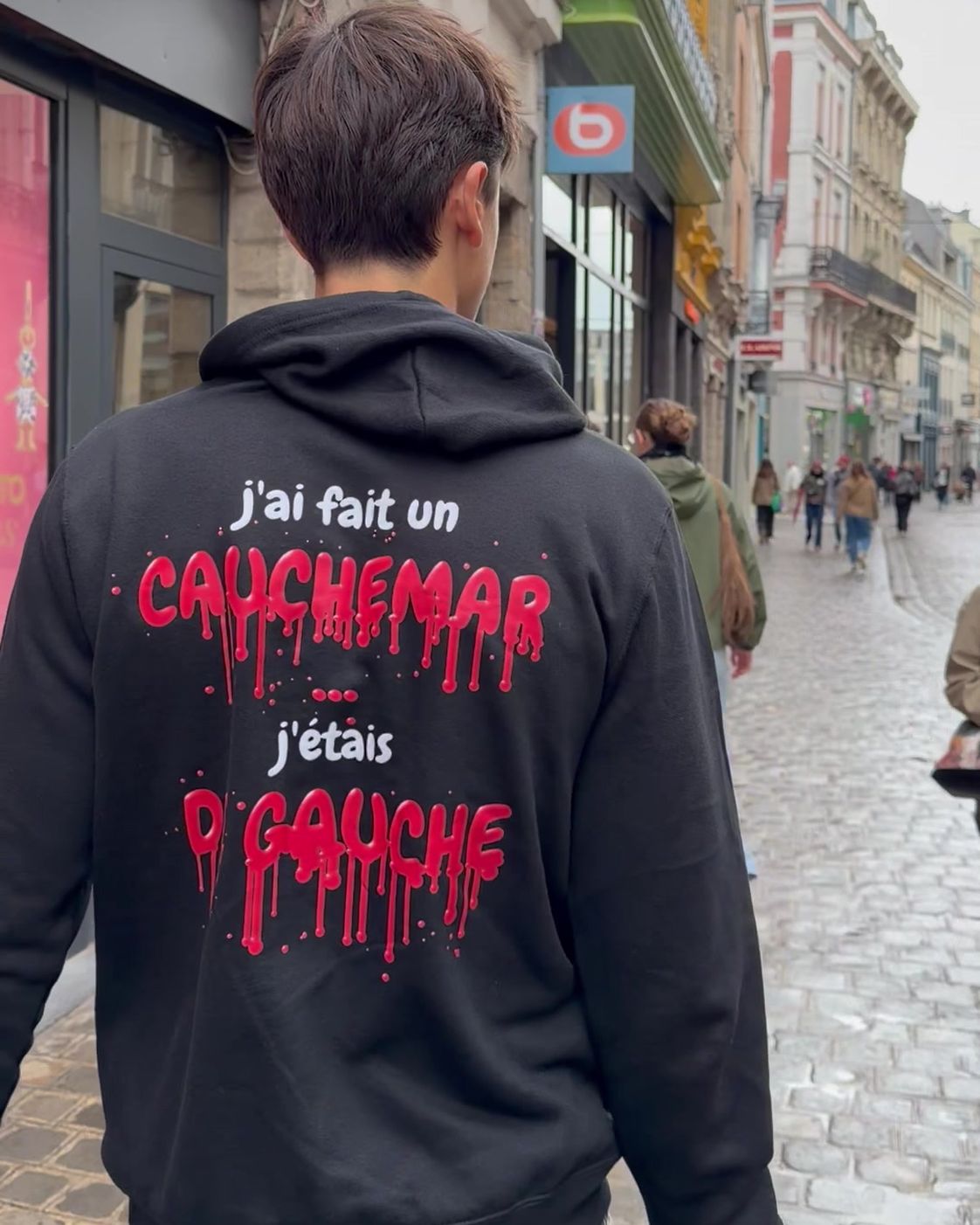 Homme de dos dans une rue commerçante de Lille portant le pull à capuche Halloween J'ai fait un cauchemar Hustle Wear, encre rouge sang