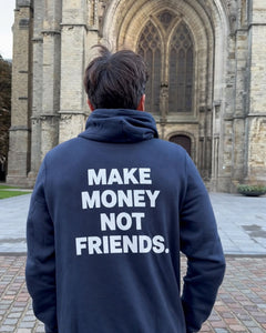 Homme de dos devant la cathédrale d'Ypres portant le pull à capuche Make Money Not Friends Hustle Wear, coloris marine
